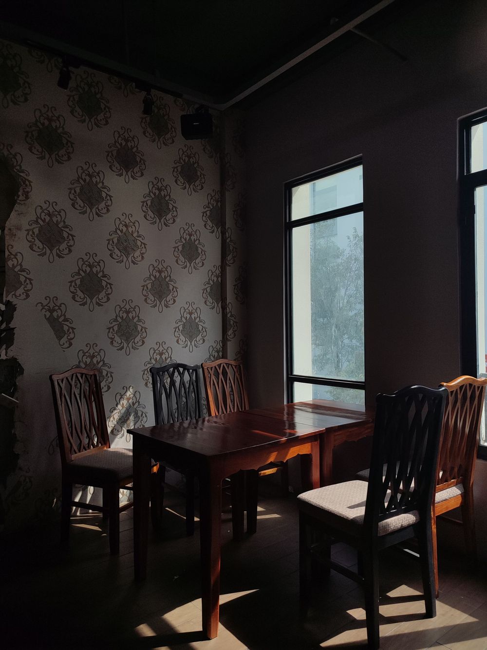 Moody dining room with ornate floral wallpaper, a dark wood table and chairs beside a tall window