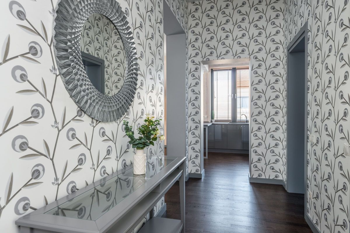 Bright hallway finished in a grey botanical leaf-print wallpaper with a round sunburst mirror and console table