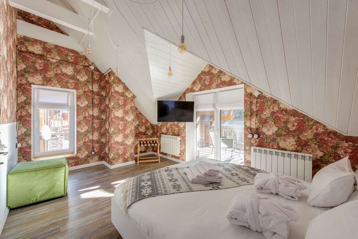 Attic bedroom with sloped white ceilings and walls wrapped in a large-scale rose floral wallpaper