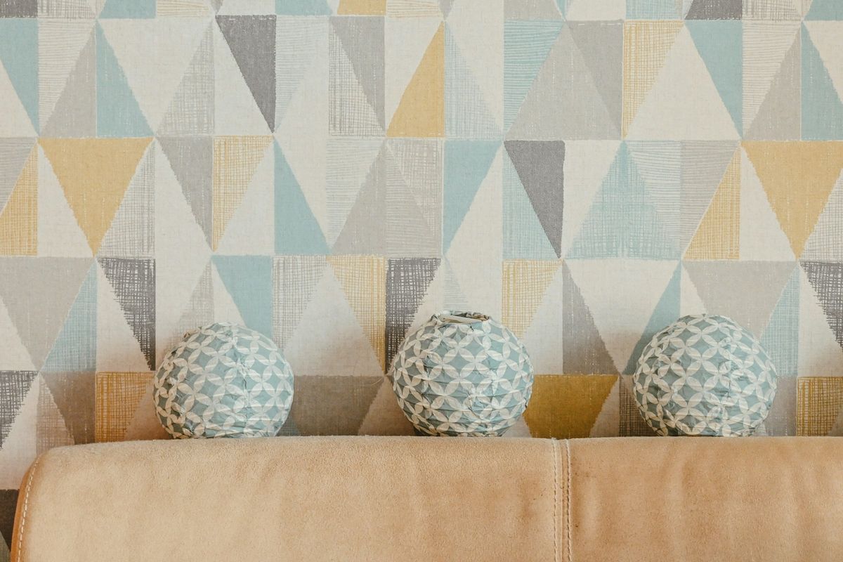 Feature wall in a pastel triangle geometric wallpaper behind a sofa with patterned cushions
