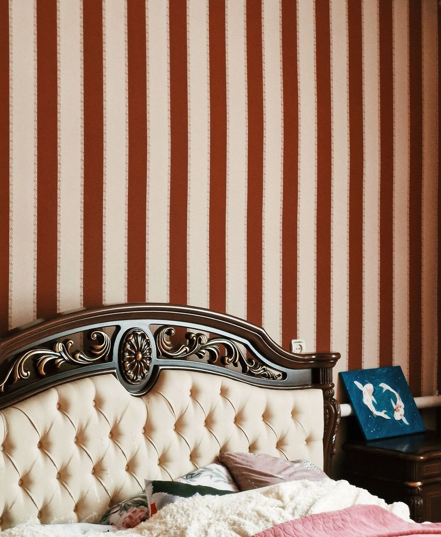 Bold red and cream striped wallpaper behind a carved, tufted bed headboard
