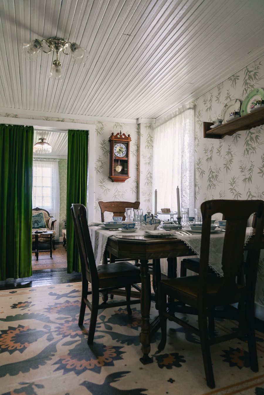 Traditional dining room with soft botanical wallpaper, dark wood chairs, green curtains and a patterned rug