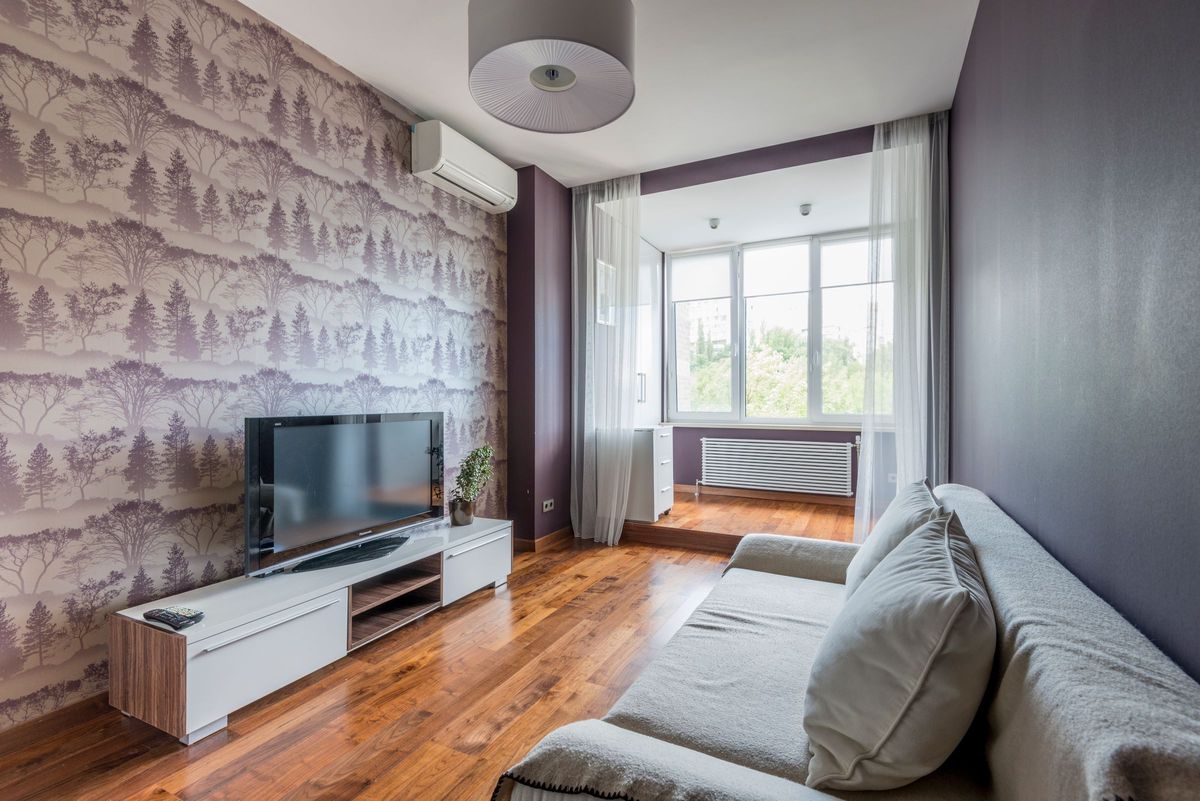 Living room with a misty forest-pattern wallpaper wall behind a media console and grey sofa